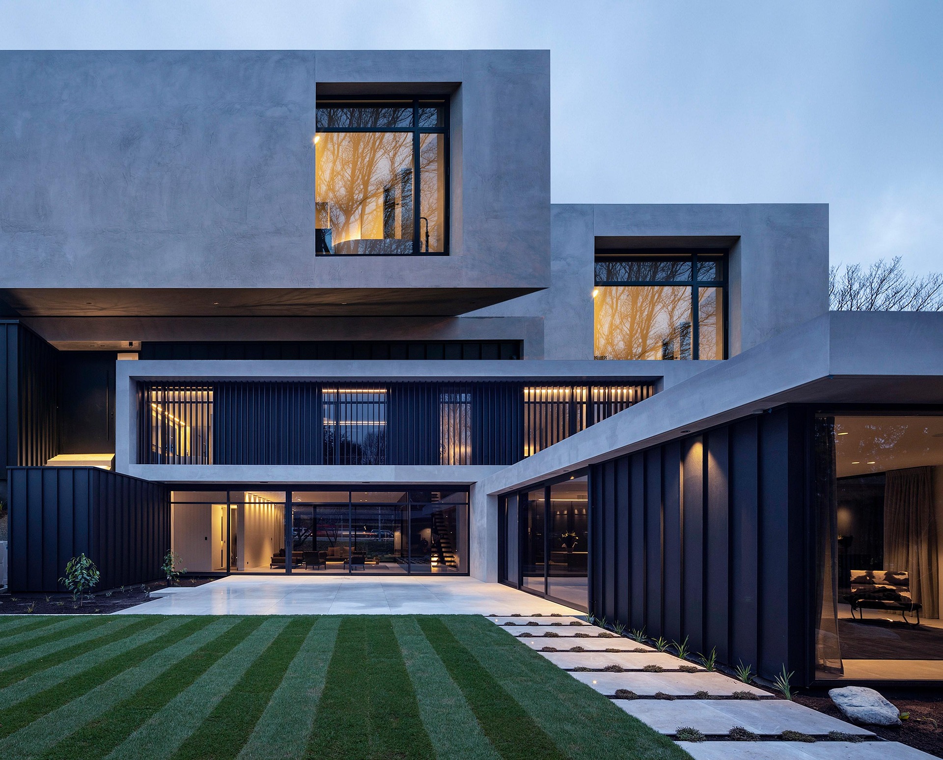 Contemporary concrete and glass residence at dusk, with warm interior light and landscaped lawn